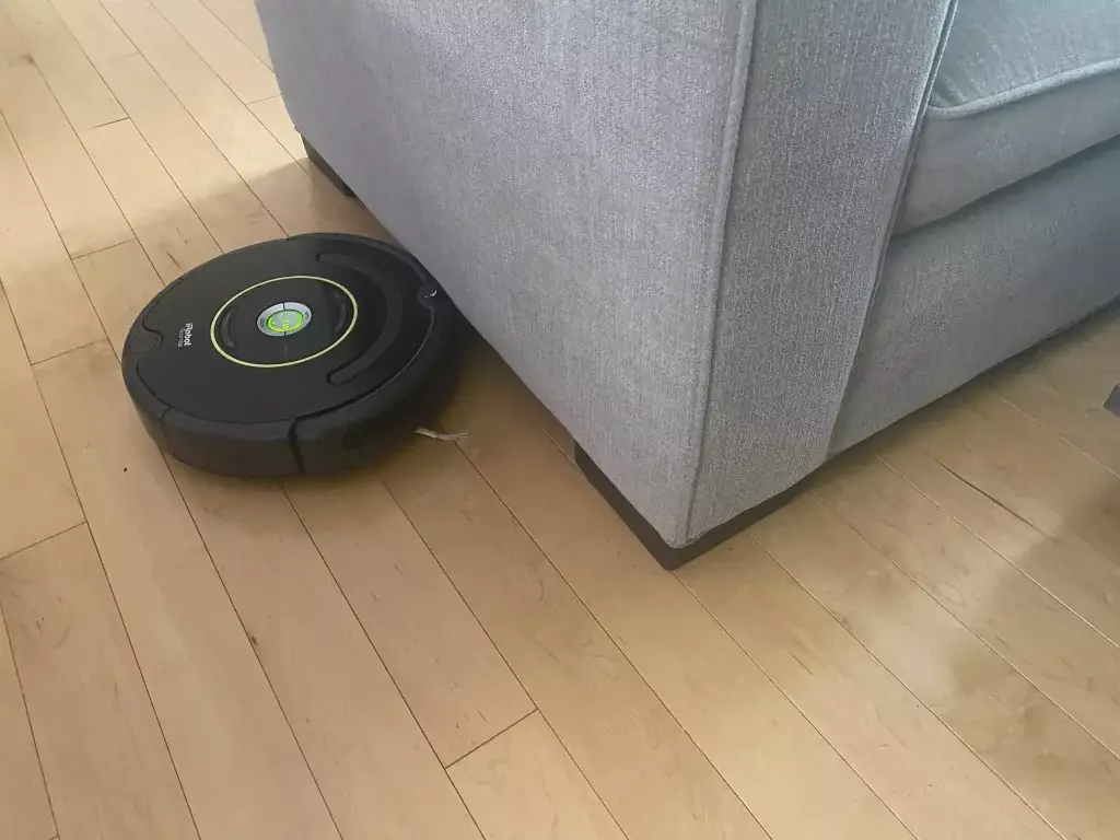 A roomba trying to clean under a couch that is too low