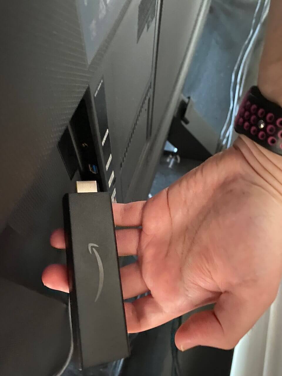 A Fire TV Stick held in front of the HDMI port where it plugs in