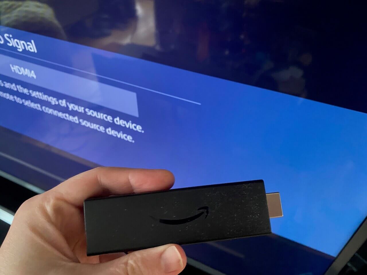 A Fire TV Stick held in front of a TV